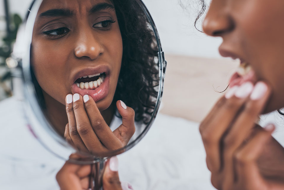 Woman looking at her gums in the mirror with pain