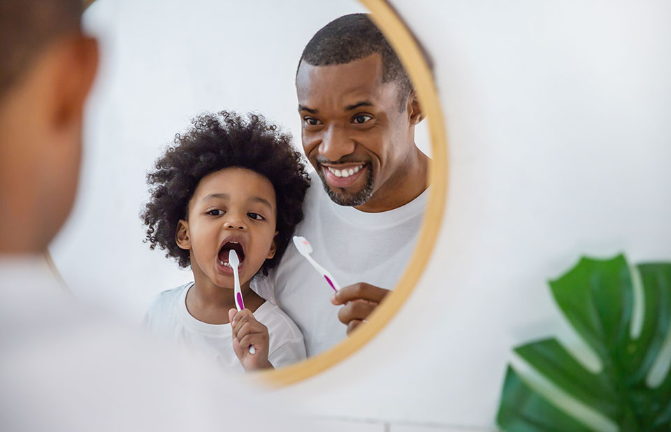 father showing his son how to brush his teeth