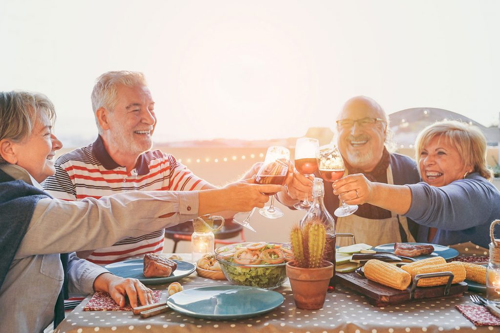 Older couples toasting with festive drinks at a holiday gathering, surrounded by food and a cheerful atmosphere, emphasizing the importance of enjoying beverages responsibly for dental health.